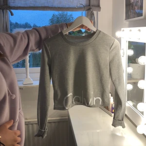 Grå Calvin Klein långermad tröja - Kort model, skönt material. Fint skick och använd ett fåtal gånger.