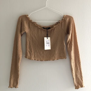 Beige stretchig topp - Har aldrig använt plagget, så prislappen sitter kvar. Toppen är kort och väldigt stretchig, den har även ganska långa ärmar. 
