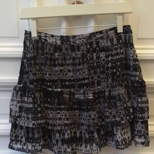  - Kort mönstrad kjol i svart/vitt med volanger. Dragkedja i sidan. Fodrad. Storlek 36