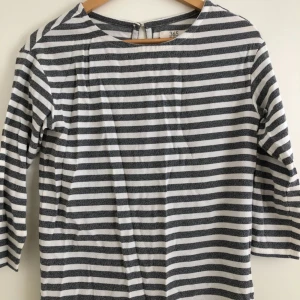  - Grå och vitrandig tröja med trekvartsärm och knapp bak i ryggen. Ganska vid modell, större än en vanlig XS i storleken.