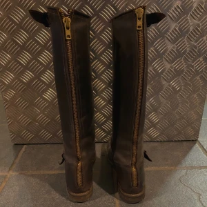 Primeboots  - Mörkbruna med guldig dragkedja. Storlek 36 men stora i storlek passar en 37. Är inte fläckiga i verkligheten, utan har skoputs på nu för att förbättra lädret.