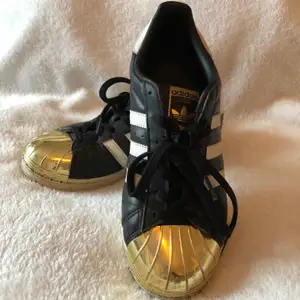 Ett par väldigt fina svarta adidas superstar med guld på framsidan, storlek 38 och 2/3 men passar på en 38-39. (Är själv 39) Väl använda och därför lite slitna på ett ställe, men i övrigt väldigt bra skick. Inköpspriset var ca.1000kr. Köparen står för frakten.💕