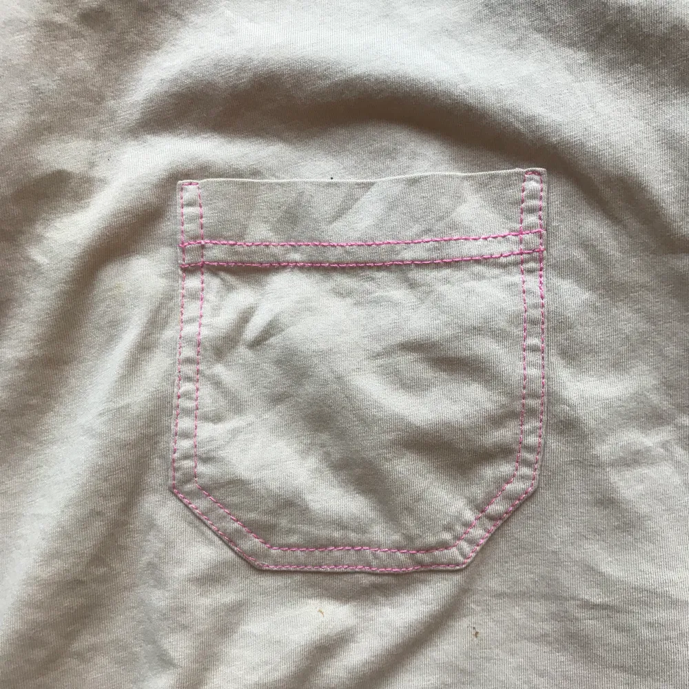 En beige t-shirt med rosa sömmar. En ficka. Använd få gånger. Passar dig med storleken sx/s. OBS: har råkat spilla tre små klorinfläckar längst ned i kanten, syns inte mycket men brukar stoppa in den i fram😊 . T-shirts.