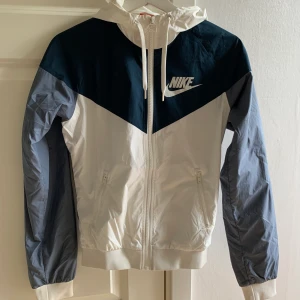 Nike Windbreaker - Nike Windbreaker i vit, mörkblå och ljusblå. Storlek XS. Använd många gånger, men är i gott skick (ej använd för träning) . Köpt för 799kr säljes för 300kr