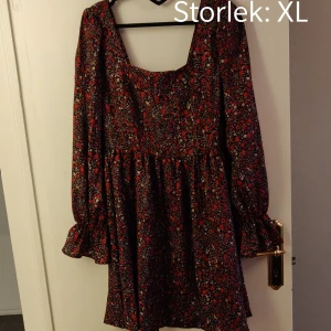 Blommig klänning - Blommig klänning i slikesliknande material, oanvänd då den är för stor för mig. "Fyrkantig" urringning och volanger vid ärmens slut 😊 Kika gärna in vad mer jag säljer! 💞