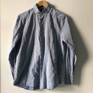  - Ljusblå skjorta med rödvita revärer 