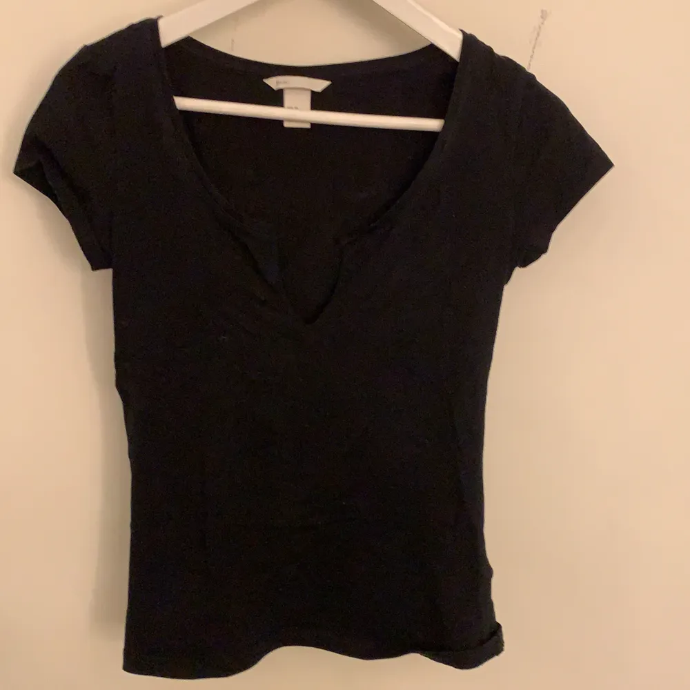 En svart t-shirt som är klippt fram vid bysten, strl XS från H&M. Använd 5-10 gånger.. T-shirts.