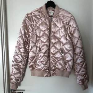 Rosa quiltad bomberjacka i satin - H&M - Rosa glansig quiltad bomberjacka i satin från HM. Grått innertyp. Använd 2 gånger. 