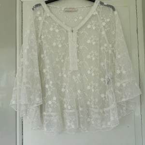 Gräddvit blus poncho  - Ponchoaktig gräddvit blus märkt L-XL men passar även mindre. Fint skick. Tror det saknas nån grej fram då det är lite trådar där, typ suttit en pärla där skulle jag tro. Sitter ihop lite innan mellan Ärm och sidan så den är inte helt som en poncho. L 65cm