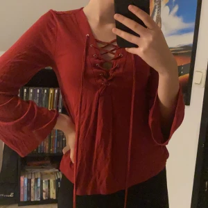 Röd tröja  - Röd tröja med snörning och utsvängda ärmar. Köpt på lager 157. Ärmarna är korta på mig som är 172. Några små hål längst ner, men de syns knappt. Frakt tillkommer.