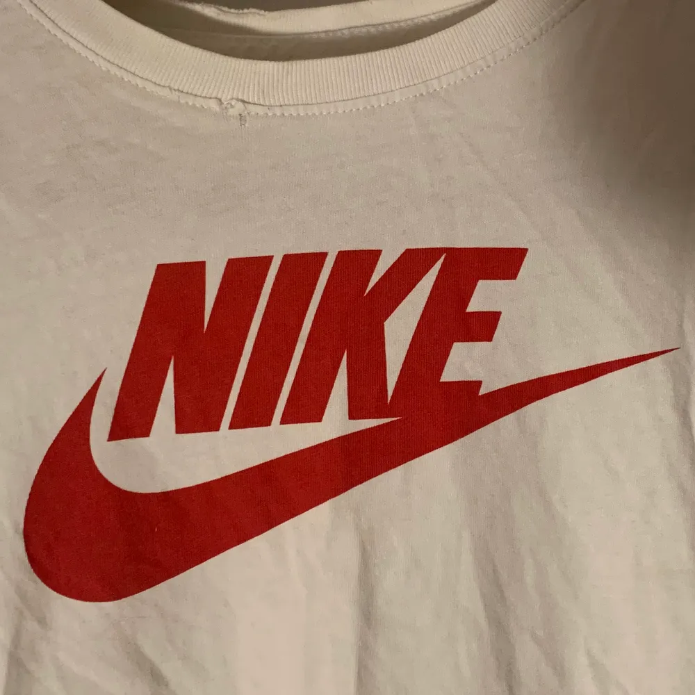 Vit Nike T-shirt med röd logga/swoosh i jätteskönt material. Strl XS. (Obs! Ser ur som en fläck vid bröstet på bilden men är som ett litet hål/tyget har blivit slitet där men syns ej när man har den på sig) . T-shirts.