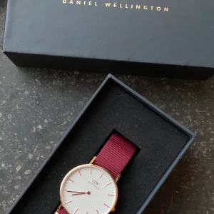 Daniel Wellington Classic Roselyn - En elegant boett, detaljer i roséguld och det traditionella NATO-bandet i rubinröd gör Classic Roselyn till en klocka som passar alla tillfällen. Endast använd vid ett tillfälle, köpt i London.   Nypris 1399:-