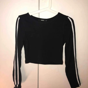  - Svart kroppad tröja med två vita ränder längst båda ärmarna.