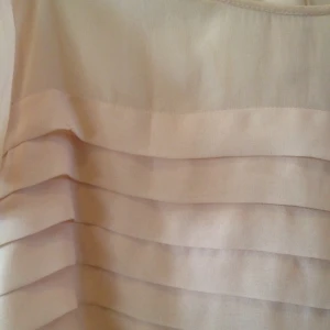 Pastellrosa t-shirt med tunnt tyg och knappar i ryggen.  - Pastellrosa t-shirt med tunnt tyg och knappar i ryggen. 