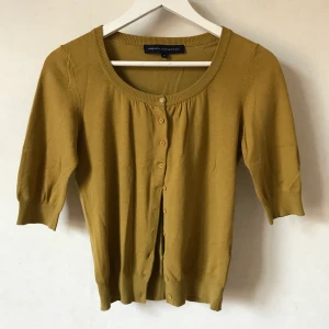 Gulgrön kofta, XS, French Connection - Supersöt trekvarts-ärmad kofta från French Connection med knappar och veckade detaljer. Liten lagning i armhåla. 75% bomull 22% polyamid 3% elastan  Kan mötas runt Stockholm/Södermalm eller skicka mot fraktkostnad! ✨🌸✨