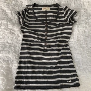 Randig tshirt  - En grå/svart och vitrandiga tshirt som aldrig är använd. Supermjukt material, snygga sömmar som detaljer, knappar över bröstet. har även hollister fågeln längst ner i hörnet. Möts upp i Stockholm, kan också frakta men isåfall står du själv för frakten. 