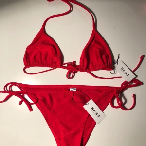 Röd bikini  - Röd bikini från Na-kd. Säljer pga att den aldrig kommit till användning, därav har den alla lappar kvar. Toppen är i strl XS, och underdelen i M, men passar en S. Fler bilder kan ges vid intresse. 