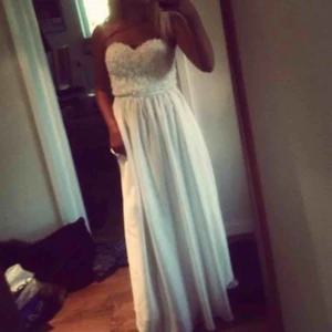 Vit lång ”balklänning” - Säljer min vackra vita långa balklänning mjuk som silke och som är använd endast en gång! Det är storlek 36 och den har ett blommönster lite likt spets upptill. Jättefint skick. Originalpris: 799 kr