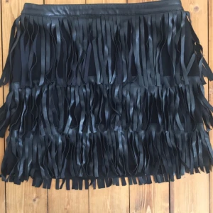  - Kort kjol med fransar i läderimitation och med dragkedja bak. Köparen står för eventuell frakt