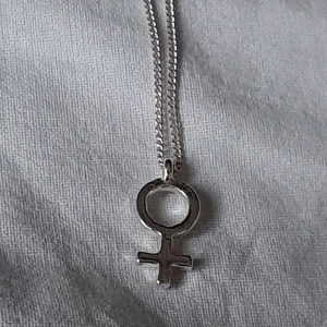  - Halsband med kvinnomärket. Små diamanter på ena sidan och slät på andra. Silverfärgad. Frakten bjuder jag på.