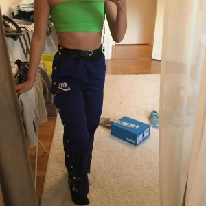  - Trackpants från förra årets Nike kollektion använda endast några gånger. Inga synliga tecken på användning utan ser nya ut.   Färg är blå med gula knappar. Resår i midjan är svart. Går använda bälte till.  Passar storlek S/M! 