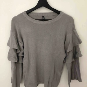  - Grå finstickad tröja med volanger på ärmarna. Endast använd 1 gång. Den är i väldigt fins skick. 