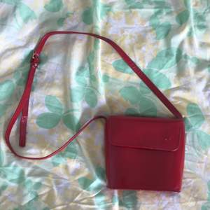 Röd lackväska! Väskan är 17 x 17 cm. Axelbandet är justerbart, men ungefär 1 meter när det är som kortast! Lite sliten men fin på utsidan! Ett stort och två små fack.