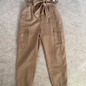 Beiga pösiga cargobyxor - Beiga cargobyxor med knytning i midjan. Använda 2 gånger. Storlek 38 och är i ett icke stretchart material.