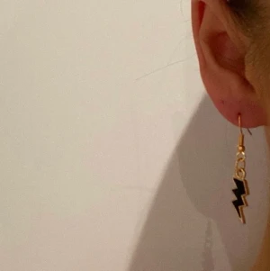 Örhänge, smycken  - X07. Jättefina örhängen med svarta och guldiga blixtrar.        Glöm inte att 10% av vinsten går oavkortat till organisationen kvinna till kvinna. 