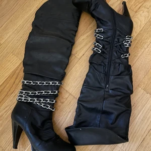 Höga knästövlar med silvrig kedja - Stövlarna är i bra skick, har andvänds 3-4 gånger så klacken är inte sliten, dem har legat på vinden 2-3 år. Storlek: 37 (jag har storlek 38 och dem passar mig).    Färg: Svart läder med silvrig dragkedja.                              Man kan välja om man vill ha dem under knäna eller över knäna (försökt visa på bilden).                                  Klackens höjd kan jag mäta vid intresse.                            Ni är jätte välkommna att prova & kolla på dem, finns i Göteborg :). 