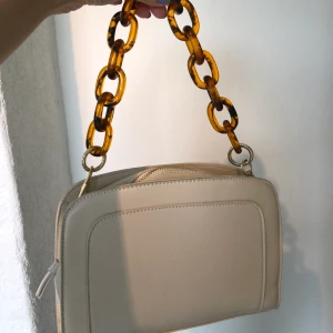 Krämvit väska  - Krämvit väska med kort band som en kedja men finns även med ett längre band om man föredrar det