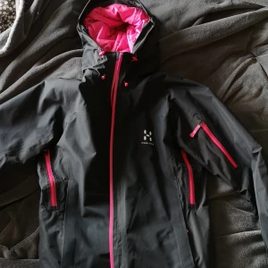 Haglöfs - Skidjacka i superskön modell. Tåler vind och väta bra och varit min favoritvinterjacka. Flera fickor både Innan på och utanpå. Svart med rosa detaljer i dragkedja och innertyg. 