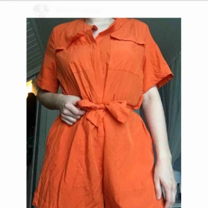  - En klarorange byxdress med knappar ifram och ett midjeband i storlek EU 40.  Använd och tvättad en gång, pga att storleken är snäppet för stor för mig.  Min info: Längd: 176cm Överdel: S/M Underdel: L/Xl
