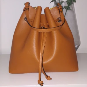  - Oanvänd väska från H&M. Lagom stor som vardagsväska.  En liten ficka finns med inuti väskan. Sitter fast med en rem. Inga skador eller slitningar. Helt nytt skick. Längre axelband finns till