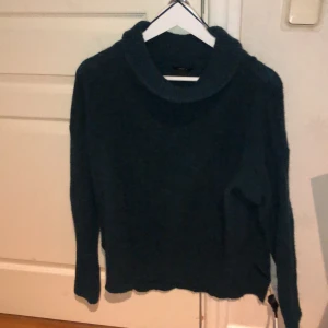 En grön stickad tröja med hög krage. - Denna Gröna stickade tröjan har en hög krage och långa arm slut. Den har också en slits på sidorna.