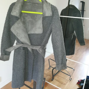 Jacka/kappa - Grå pälsjacka 2 i en, ena sidan med lurvig päls två fickor skärp. Andra sidan slät med två fickor och skärp. Mycket praktisk och jätte fin