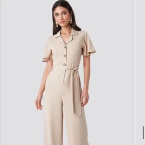 Beige Jumpsuit från NA-KD - Jumpsuit från nakd i jättefint skick, korta ärmar och vida ben med knyte i midjan!