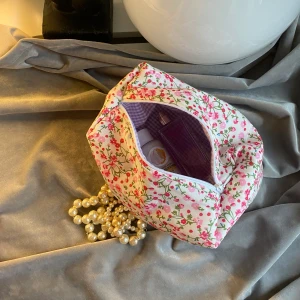 Blommig necessär - Necessär med blommor som yttertyg,ett vitt mellantyg(syns inte)och lila rutigt innertyg. Ca 19cm lång,11cm bred och 10 cm hög. Jag hobbysyr bara så kan inte lova raka sömmar eller 100% felfritt. Skickas med frimärke: 22kr och filmar när den skickas. Är din för 100kr plus porto