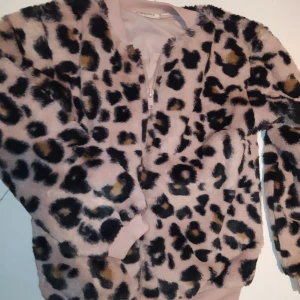 Fuskpäls jacka till det lilla modelejonet! - Strl 110/116, riktigt fint skick! Puderrosa och leoprint. Märke Kappahl. Passar till vår och sommar eller inomhus. Djur och rökfritt hem. Samfraktar gärna,kika på mina övriga annonser!