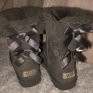 Gråa uggs - Gråa uggs med rosetter i storlek 37, köpta på tradera för någon månad sedan för 600kr men inte använda av mig då de är för stora, därav det låga priset