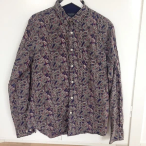  - Skjorta från East West i fint paisleymönster och i nyskick.   Storlek L. Dold button down.