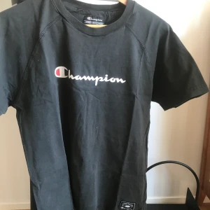 90s Champion t-Shirt Svart - Vintage Champion t-shirt från 90-talet som har väldigt ”tjockt” material/tyg och bred halskrage. Sitter snyggt och är inte tajt