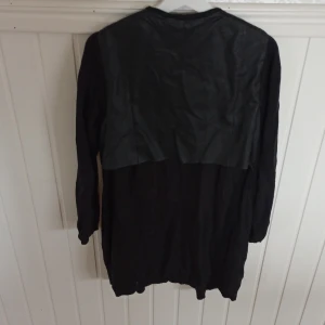 Lång kofta med konstläderdetalj på rygg - Lång svart kofta med detalj av konstläder. Fint skick.