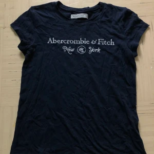 Abercrombie and Fitch t-shirt - En marinblå abercrombie and fitch tröja, kortärmad. Använd några gånger men väldigt fin kvalitet, mjukt tyg och skön att ha på sig. Den har tyvärr blivit för liten, så inga hål eller fläckar. 