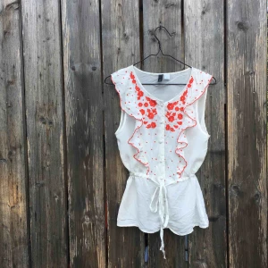  - Somrig kortärmad blus med orange broderier och knyt i midjan. Smickrande passform. 