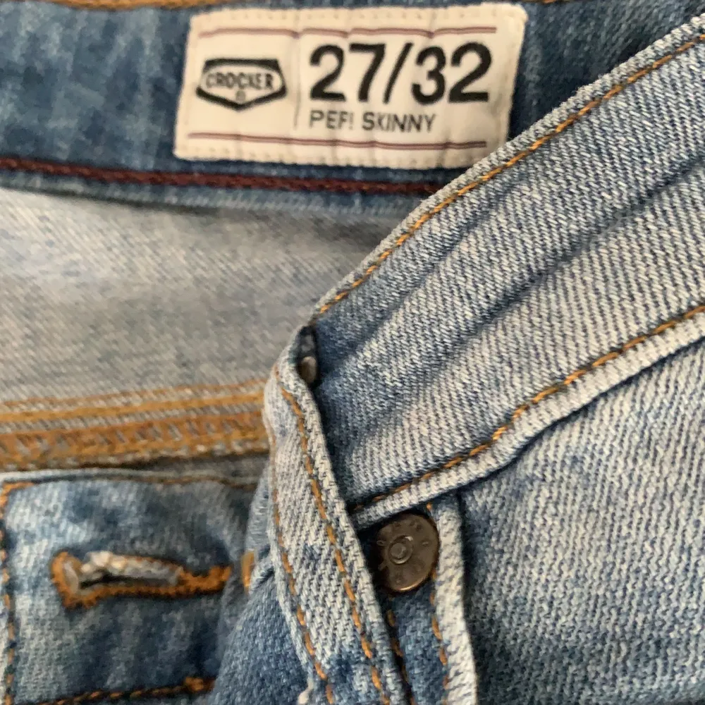 Ett par lågmidjade ljusblåa jeans från Crocker, med hål på knäna. Storlek 27/32. Jeans & Byxor.