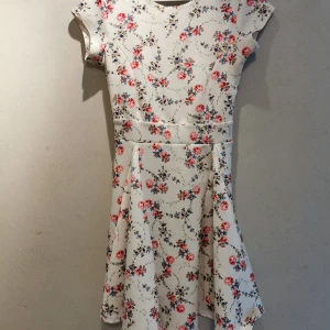 Blommig skater klänning - Jättefin blommig klänning med vit bakgrund i skater dress format. Något tjockare tyg, utan dragkedja men väldigt stretchig. Använd en del gånger och har några märken på kjolen som jag ej vet vart de kommer ifrån (se bild), syns ej på långt håll. 
