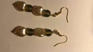 Guld örhängen, gröna & pärlor i form av hjärtan - 2 guldiga örhängen. 1 par örhängen kostar 30kr och båda kostar då 60kr. Gröna små gulliga klädnypor. Och ett par med gröna pärlor och vita pärlor som är hjärtformade :)