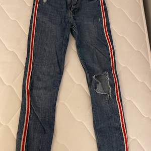 Ett par skitsnygga jeans med röd rand på sidorna och snygg slitning på knäet. Aldrig använda utan har bara legat i garderoben och tagit plats. köpare står för frakt, kontakta för fler bilder eller frågor