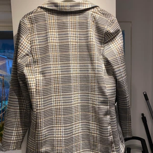 Kavaj storlek M - En grå rutig kavaj med två stora fickor framtill. Lätt att matcha och perfekt till våren! Säljes på grund av lite för liten